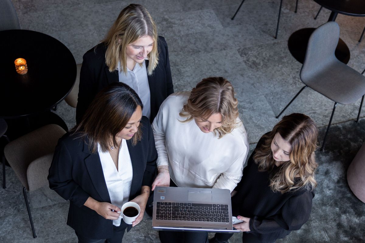 fyra kvinnor står samlade runt bärbar dator