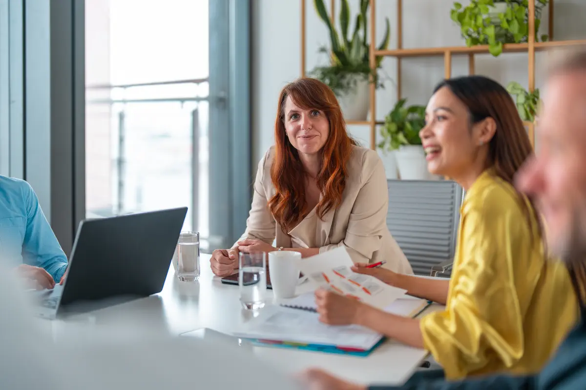 rödhårig kvinna sitter i möte och ler mot kameran